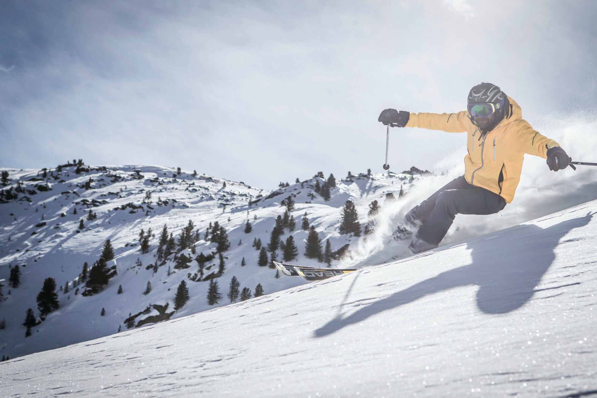 Skifahrer mit gelber Skijacke unterwegs auf der Piste - AHRIA Apartments