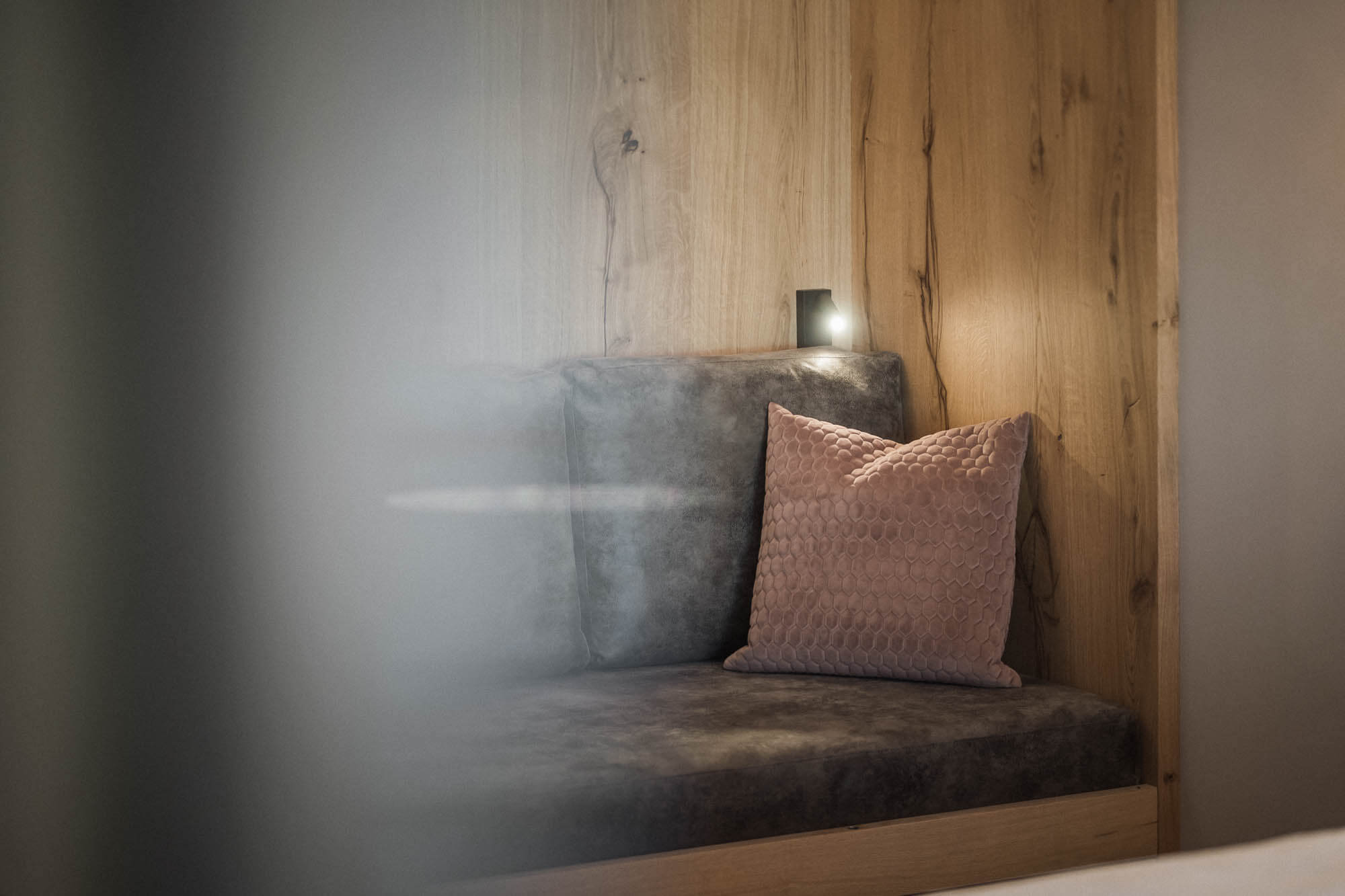 Graues Sofa mit rosa Kissen und Holztäfelung im AhriaPura Apartment - AHRIA Apartments