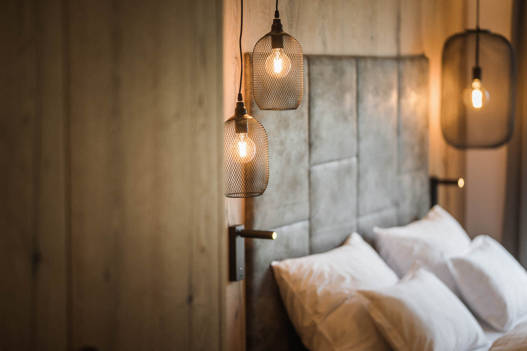 Kopfseite vom Doppelbett mit mehreren Kissen und schwarzen Hängelampen im AhriaPura Apartment - AHRIA Apartments