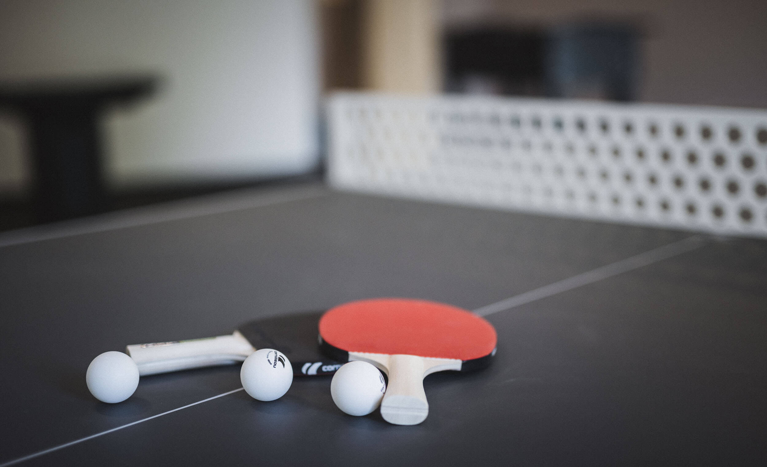 Tischtennisschläger und -bälle liegen auf einer Tischtennisplatte im AhriaPura Apartment - AHRIA Apartments