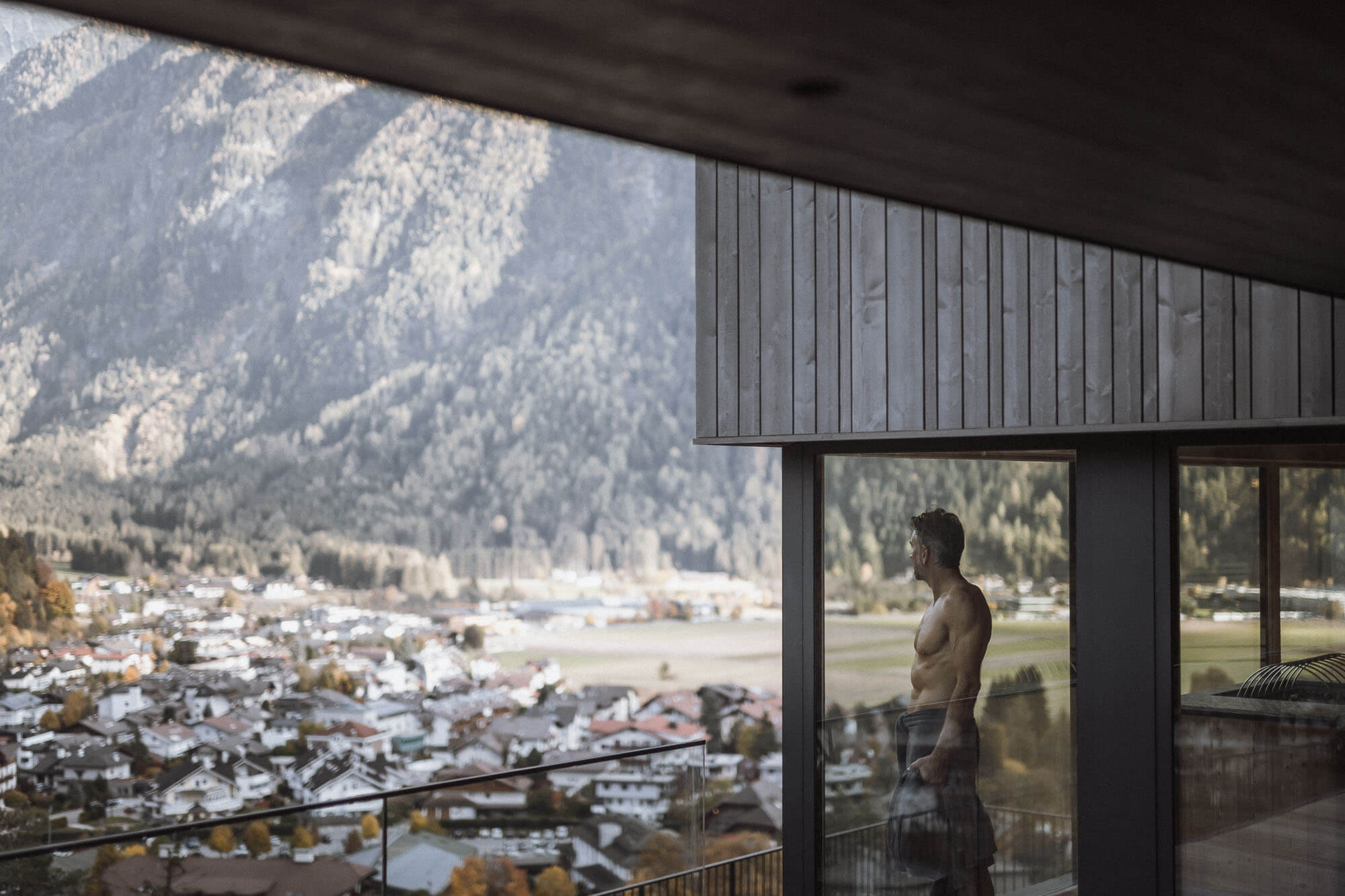Mann steht auf dem Balkon nach einem Saunadurchgang und blickt auf Sand in Taufers - AHRIA Apartments