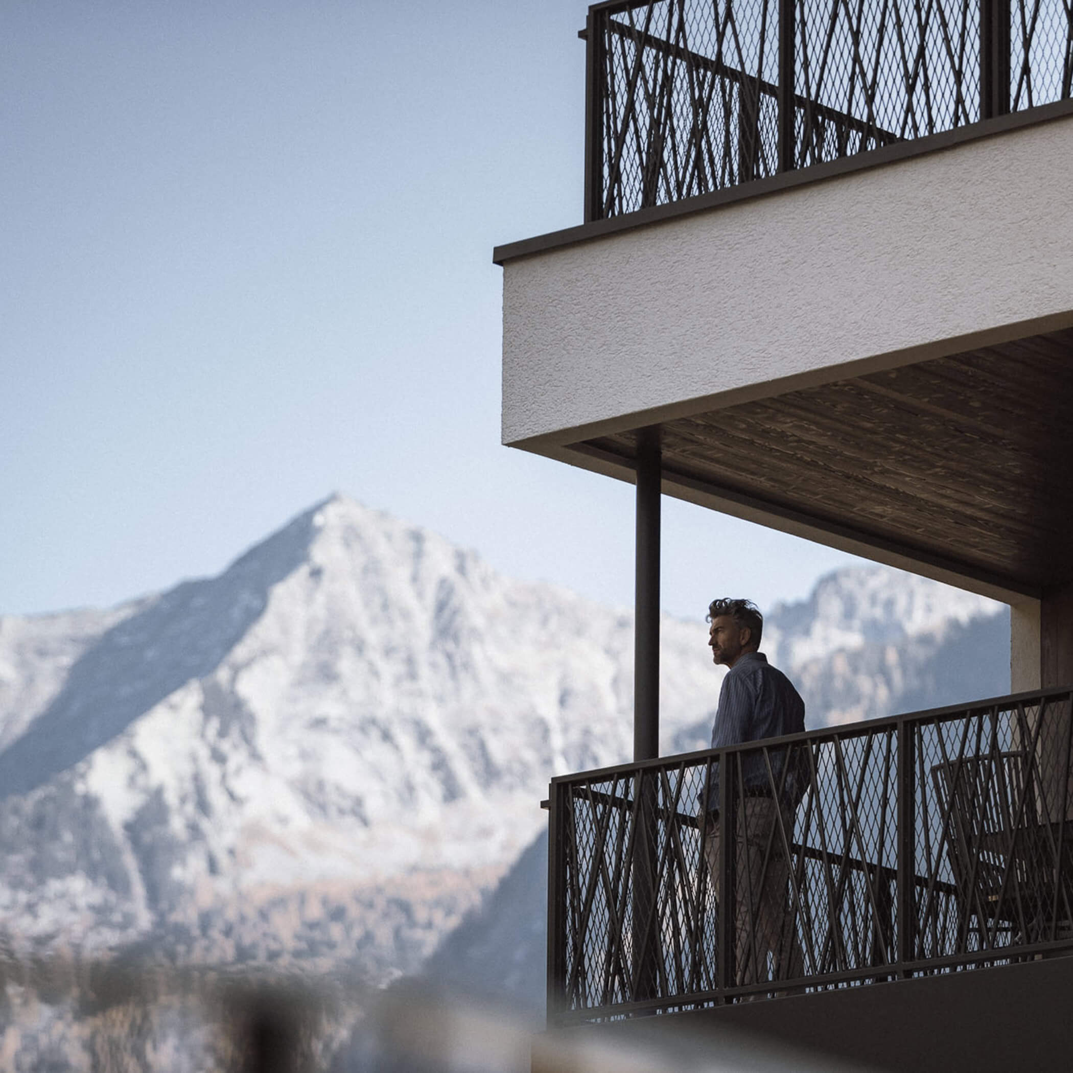 Un uomo si trova sul grande balcone e si gode la vista del paesaggio montano - AHRIA Apartments