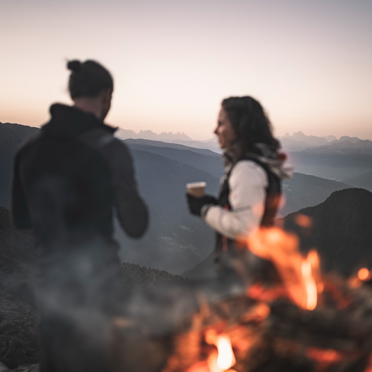 Eine Frau und ein Mann warten an einem Lagerfeuer auf den Sonnenaufgang - AHRIA Apartments